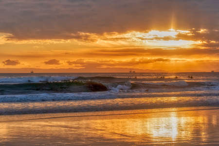 A beach surrounded by the wavy sea under a cloudy sky during a golden sunsetの写真素材