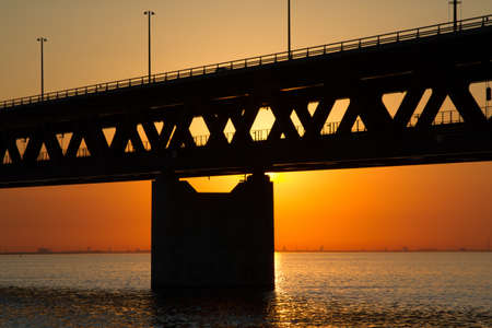 A silhouette of a bridge over the sea with an orange sky in the backgroundの写真素材