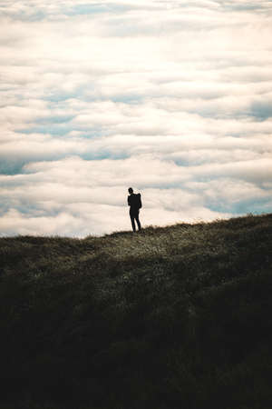 A silhouette of a person standing on a grassy hill with a cloudy sky in the background