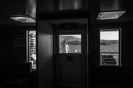 A woman, a girl and a man seen through the windows of an apartment in front of the waterの写真素材