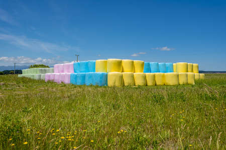 A grassy field with hay bales wrapped in colored polytheneの写真素材