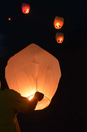 A vertical shot of a person flying wishing lanterns into the night sky