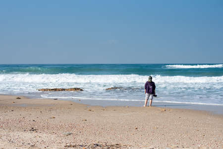 PALMACHIM BEACH, ISRAEL - Dec 15, 2019: A girl standing on the beach surrounded by the sea under a blue sky and sunlightのeditorial素材