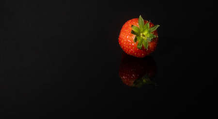 A strawberry reflecting in a glass with a black backgroundの写真素材
