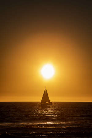 A vertical shot of the sun setting over the  boat sailing in the oceanの写真素材