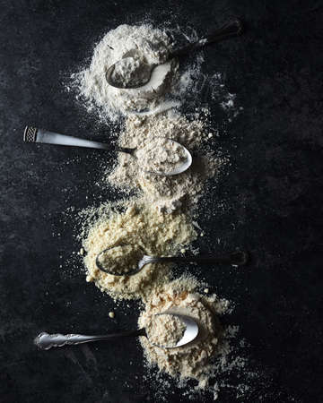 A vertical shot of four spoons in a white flour on a black backgroundの写真素材