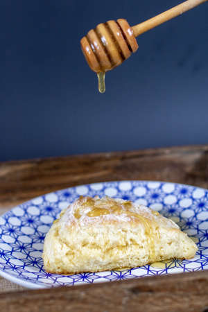 A vertical shot of a scone on a plate while putting honey on topの写真素材