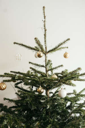 A vertical shot of a Christmas tree decorated with golden baubles against a white wallの写真素材