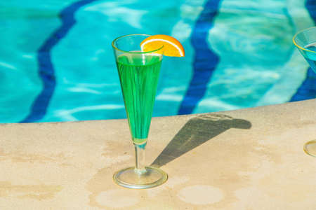 A closeup shot of a green cocktail near the pool on a sunny dayの写真素材