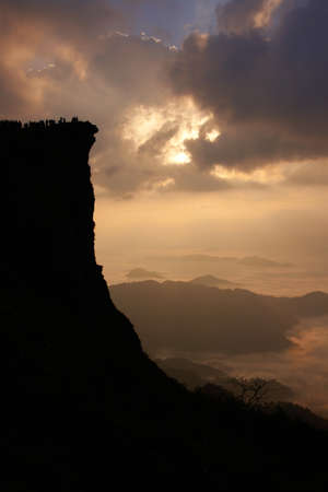 A silhouette of people standing on top of a cliff above the clouds in Northern Thailand