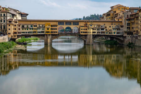 The beautiful Ponte Vecchio bridge in the foreground of high buildings reflected in the lake in Florence, Italyのeditorial素材