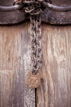 A vertical closeup shot of an old wooden gate with a rust iron lock and chainsのeditorial素材