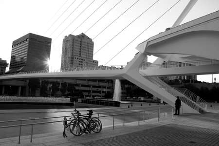 A gray scale shot of a bridge, some bikes and buildings in the background