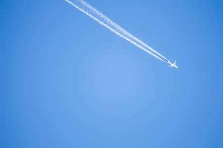 A beautiful shot of a white airplane flying and leaving its trail in the clear blue skyのeditorial素材