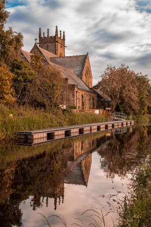 A vertical shot of a brown castle by a lake surrounded with trees and grass under a cloudy skyのeditorial素材