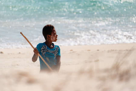 AMBATOMILO, MADAGASCAR - Aug 15, 2019: A kid playing alone on the beach with a stick