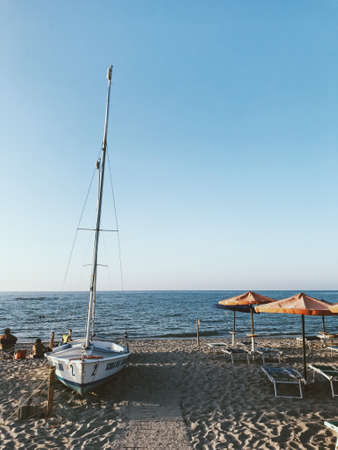 A vertical shot of a white sailboat on the shore near the water with a blue sky in the backgroundのeditorial素材