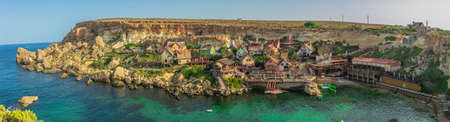 A panoramic shot of a lot of houses on the shore of the calm sea near a cliff under the blue skyのeditorial素材