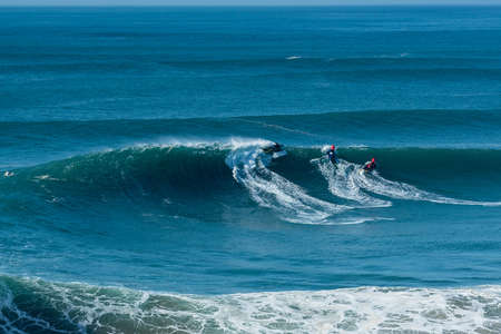 NAZARÃ©, PORTUGAL - Dec 01, 2019: The surfers riding on the waves of the Atlantic Ocean toward the shore at Nazare, Portugalのeditorial素材