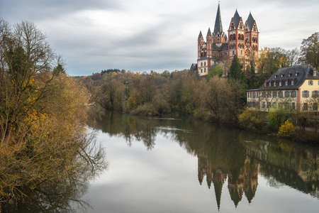The Limburg cathedral surrounded by greenery reflecting on the river under a cloudy sky in Germanyのeditorial素材