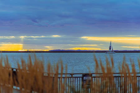 BUFFALO, UNITED STATES - Jun 11, 2018: A sailboat out on the lake from a lakeshore view. Beautiful sunset with blue water and dark clouds.のeditorial素材