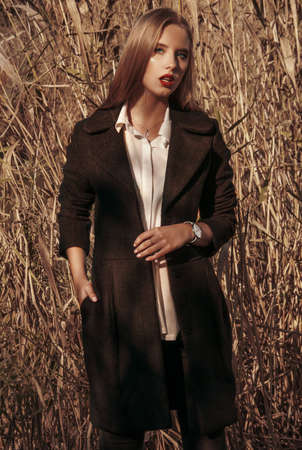 KYIV, UKRAINE - Sep 30, 2019: A vertical shot of a beautiful blonde female wearing a long coat standing in the field of dry grassのeditorial素材