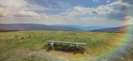A panoramic shot of a wooden bench in the field in Charinthia, Slovenia with a rainbow on the right...