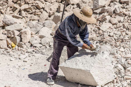 A hardworking worker breaking the stones with a hammer captured on a hot sunny dayの写真素材