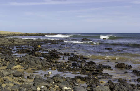 A beach covered in rocks surrounded by the sea under sunlight and a blue sky in Spain