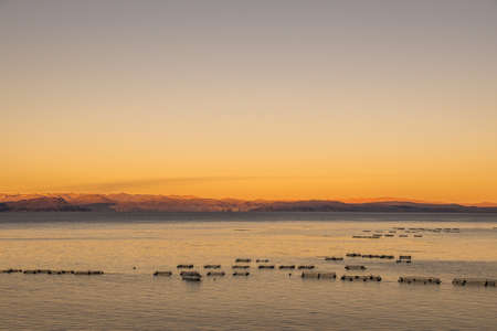 A high angle shot of the calm surface of the ocean with the mountains in the background at sunsetの写真素材