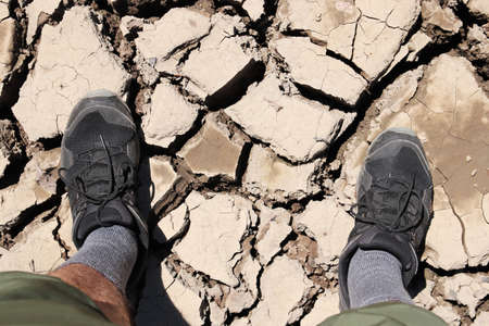 A high angle shot of a person standing on the dried and cracked muddy ground
