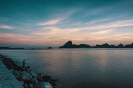 The sea surrounded by rocks under a cloudy sky during a beautiful sunsetの写真素材