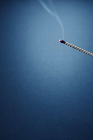 A vertical shot of a burnt matchstick with a blue wall in the backgroundの写真素材