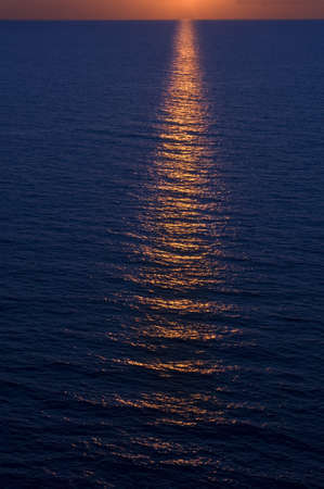 A vertical picture of the sea with the sunset reflecting on the water in the eveningの写真素材