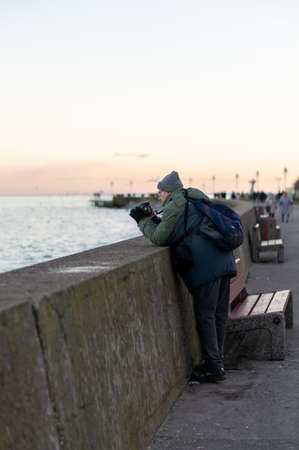 GDYNIA, POLAND - Jan 05, 2020: Man taking a photo with his camera by a barrier at the seaside on a...
