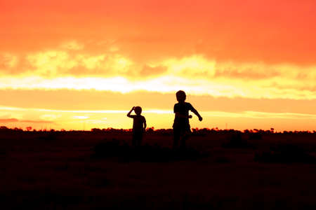 The silhouettes of children running through a field during the golden sunsetの写真素材