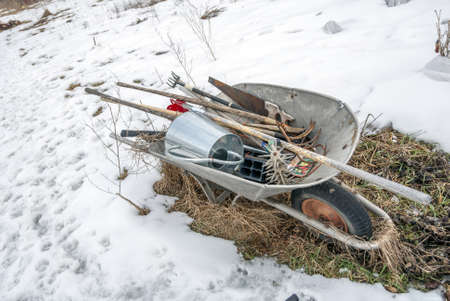 A closeup shot of a wheelbarrow with several metal instruments placed inside surrounded by snowの写真素材