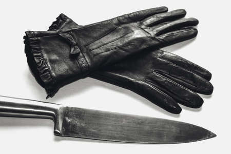 An overhead shot of black gloves and a metal knife on a white surface