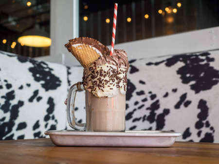 A chocolate milkshake with a waffle on it on a tray in a cafe with a blurry background