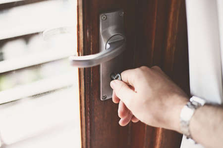 A closeup shot of a person turning the key in the lock of the wooden doorの写真素材