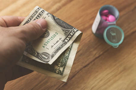 A high angle shot of a person holding a dollar bill over some pills on a wooden surface