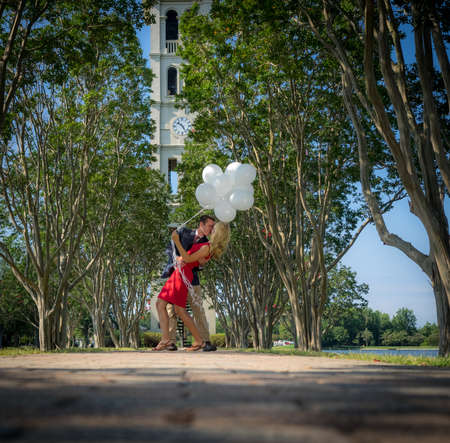 A kissing couple with balloons in a garden surrounded by trees under the sunlightの写真素材