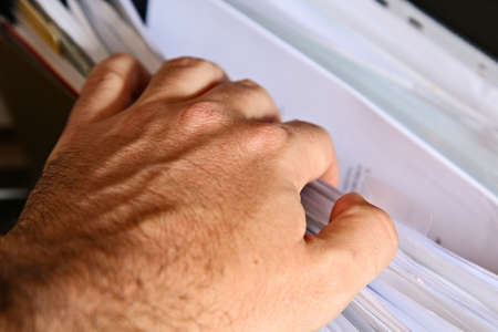 A Caucasian man looking inside a filing cabinet for tax records.  Administration concept image.