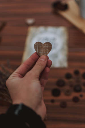 A closeup shot of a man holding a heart shaped wood in his hands over a brown patterned table
