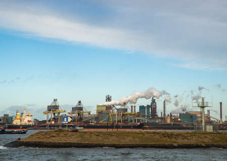A sea with boats ailing and a big factory in the distance under a blue skyの写真素材