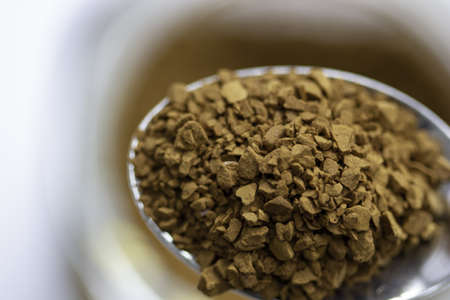 A closeup of instant coffee grains in the spoon with a cup on the blurred backgroundの写真素材