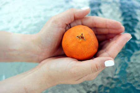 A closeup shot of a female hand holding a wrinkled orange a swimming poolの写真素材