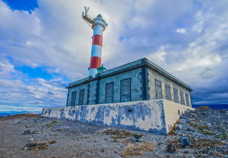 A low angle shot of a lighthouse beside the small building with a cloudy blue sky of canary islands in spainの写真素材