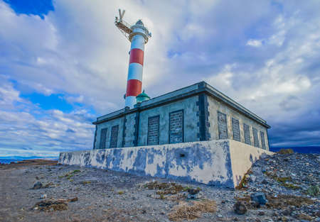 A low angle shot of a lighthouse beside the small building with a cloudy blue sky of canary islands in spainの素材 [FY310155890242]