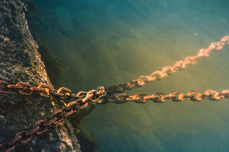 A high angle closeup shot of rusty chains sunk in the waterの写真素材